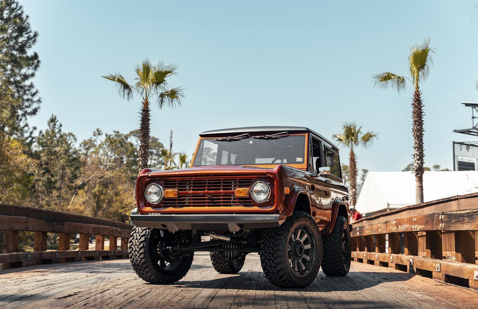 A brown jeep is parked on a dirt road next to palm trees