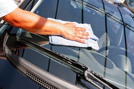 Person wiping a car windshield with a blue cloth; sunny day.
