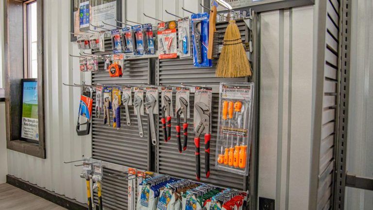 A retail display rack holds various hand tools including pliers, wrenches, screwdrivers, and a small broom.