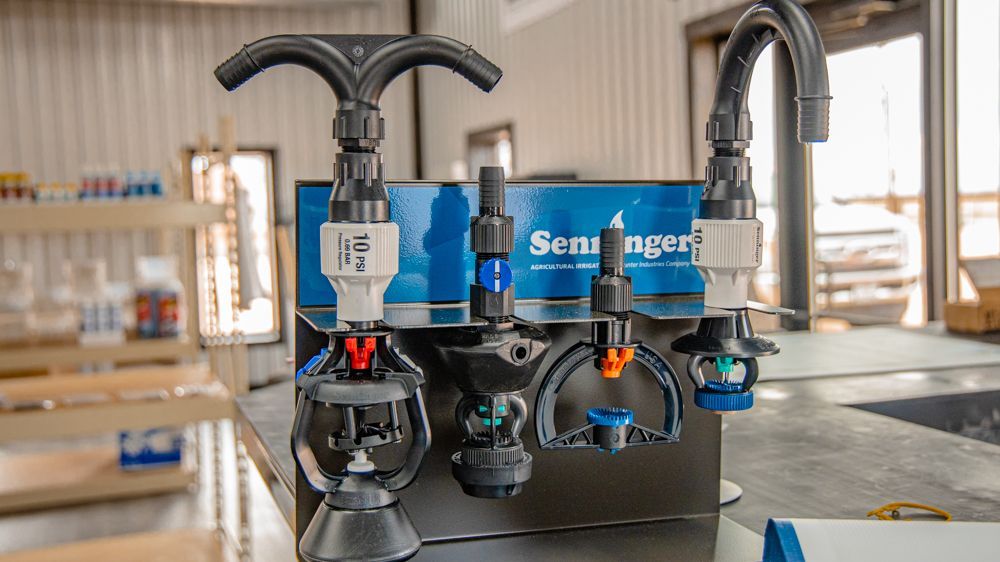 A retail display of Senninger irrigation sprinkler heads mounted on a blue branded stand in a warehouse setting.