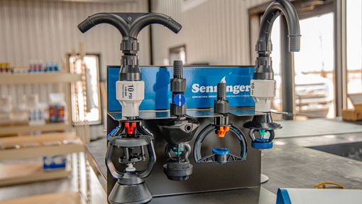 A retail display of Senninger irrigation sprinkler heads mounted on a blue branded stand in a warehouse setting.