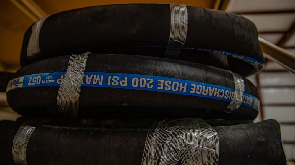 A stack of black water discharge hoses with blue labeling stating 