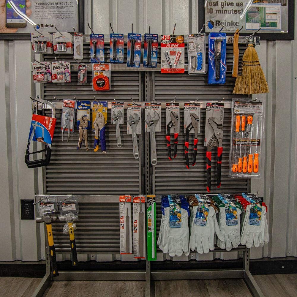 A retail display rack filled with various hand tools, including wrenches, pliers, screwdrivers, gloves, and a broom.