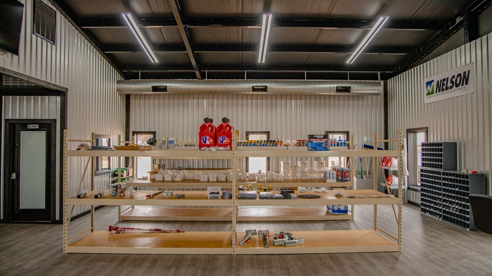 A bright workshop or retail space featuring wooden shelving filled with various tools, parts, and supplies.