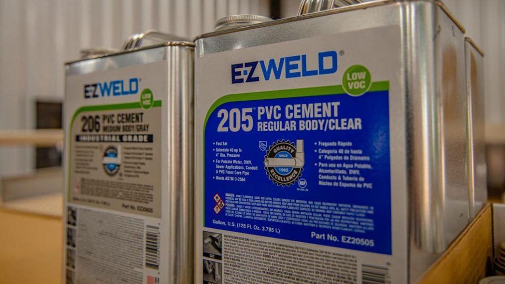 Two metal cans of EZWELD PVC cement on a flat surface, with a 206 grey industrial grade can and a 205 clear regular body can.