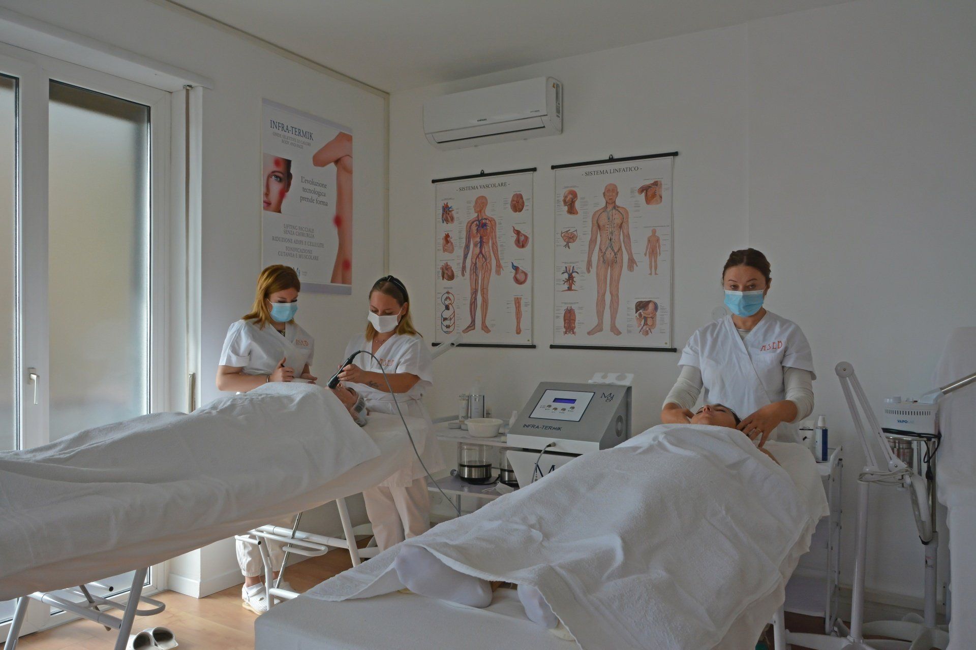 Tre persone con la mascherina e il camice bianco azionano delle apparecchiature sui pazienti sdraiati sui letti di una clinica.