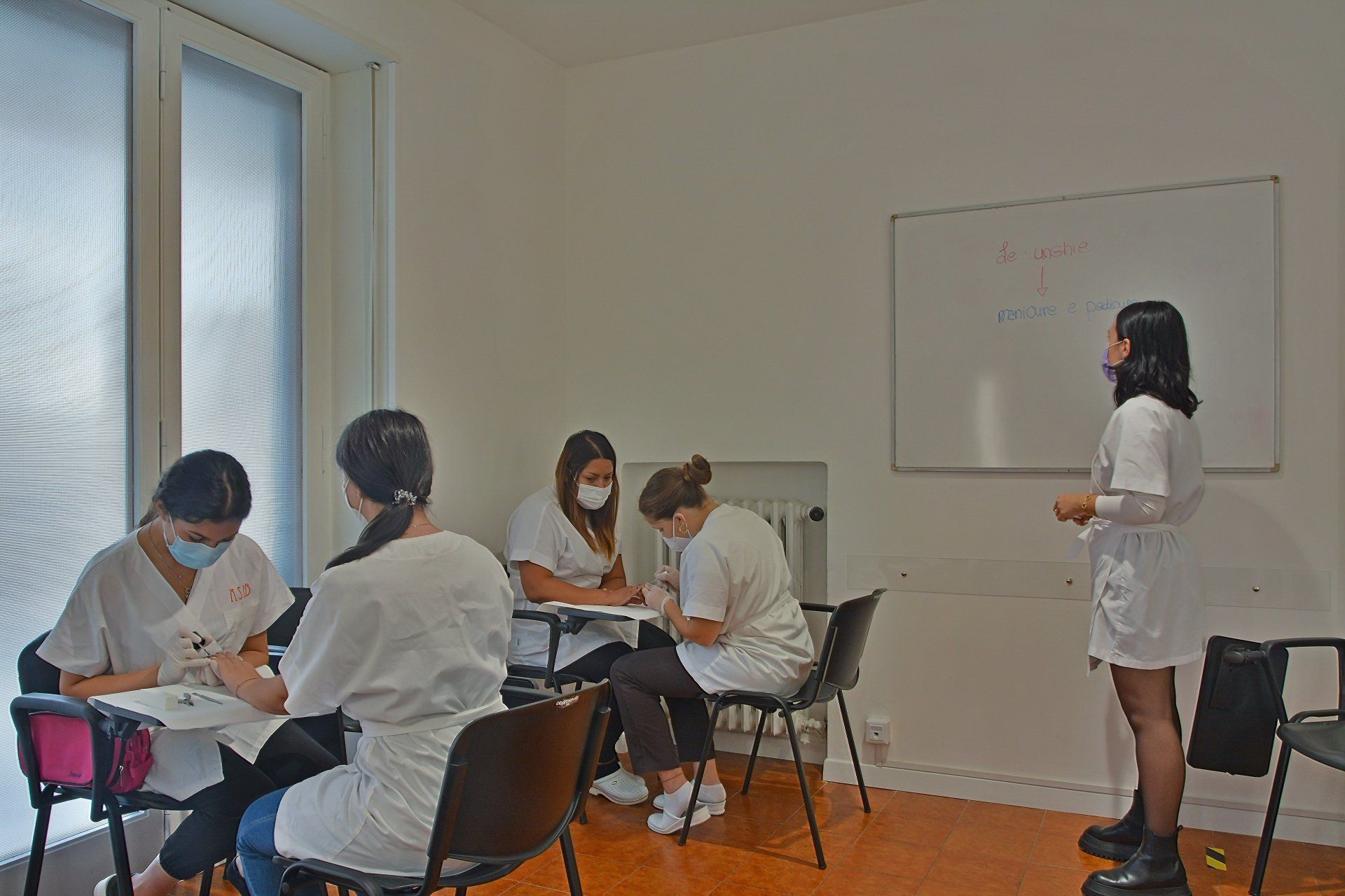Persone in camice bianco partecipano a un corso per onicotecnici, spiega una donna.