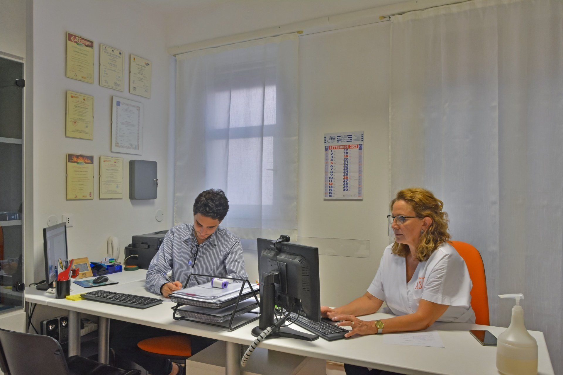 Due persone lavorano alla scrivania in un ufficio; una scrive, l'altra scrive. Ambiente d'ufficio.