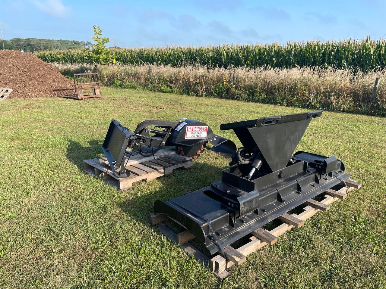 Two pieces of equipment are sitting on wooden pallets in a grassy field.