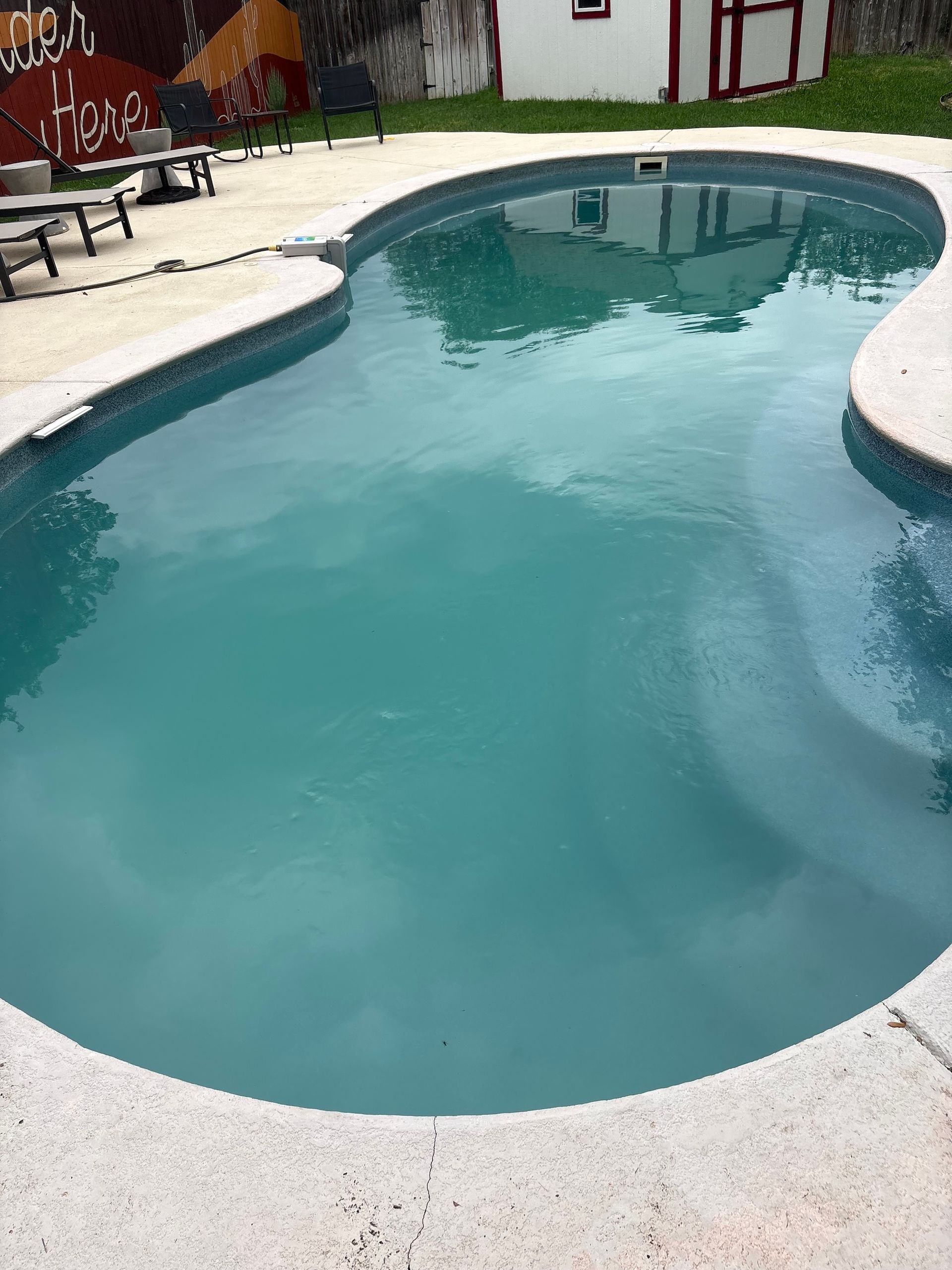 Curved backyard swimming pool with turquoise water and white deck, chairs along the left side