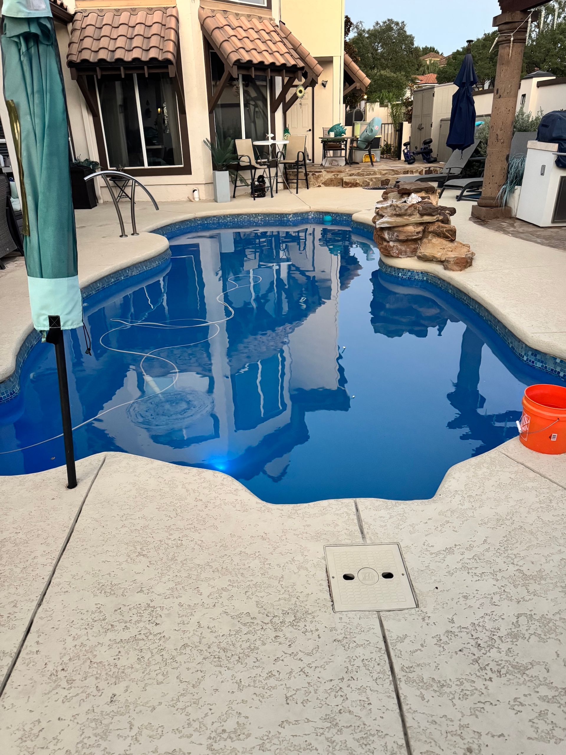 Backyard pool filled with bright blue water beside patio furniture and houses