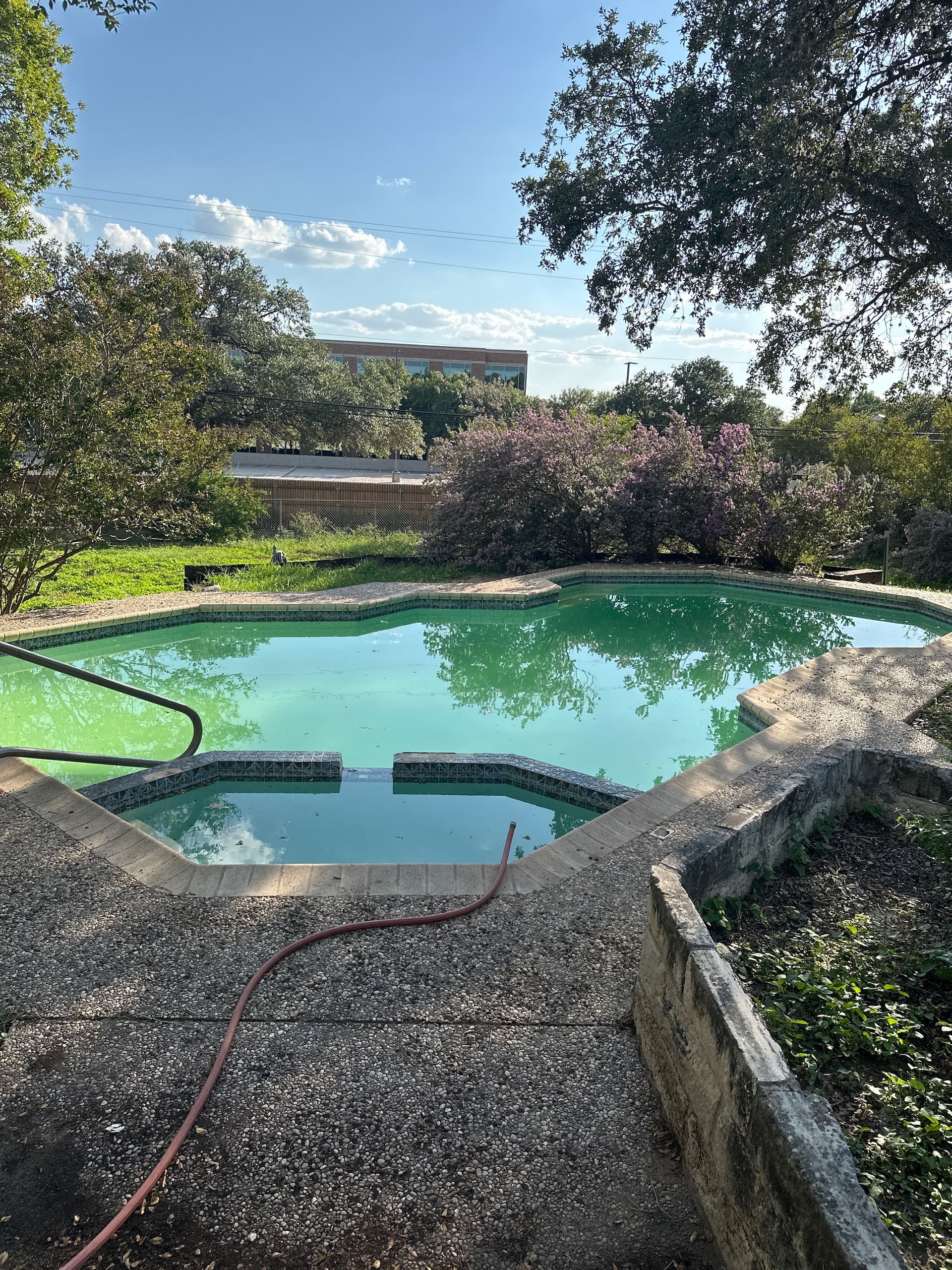 Backyard pool with turquoise water, gravel deck, and trees under a sunny sky