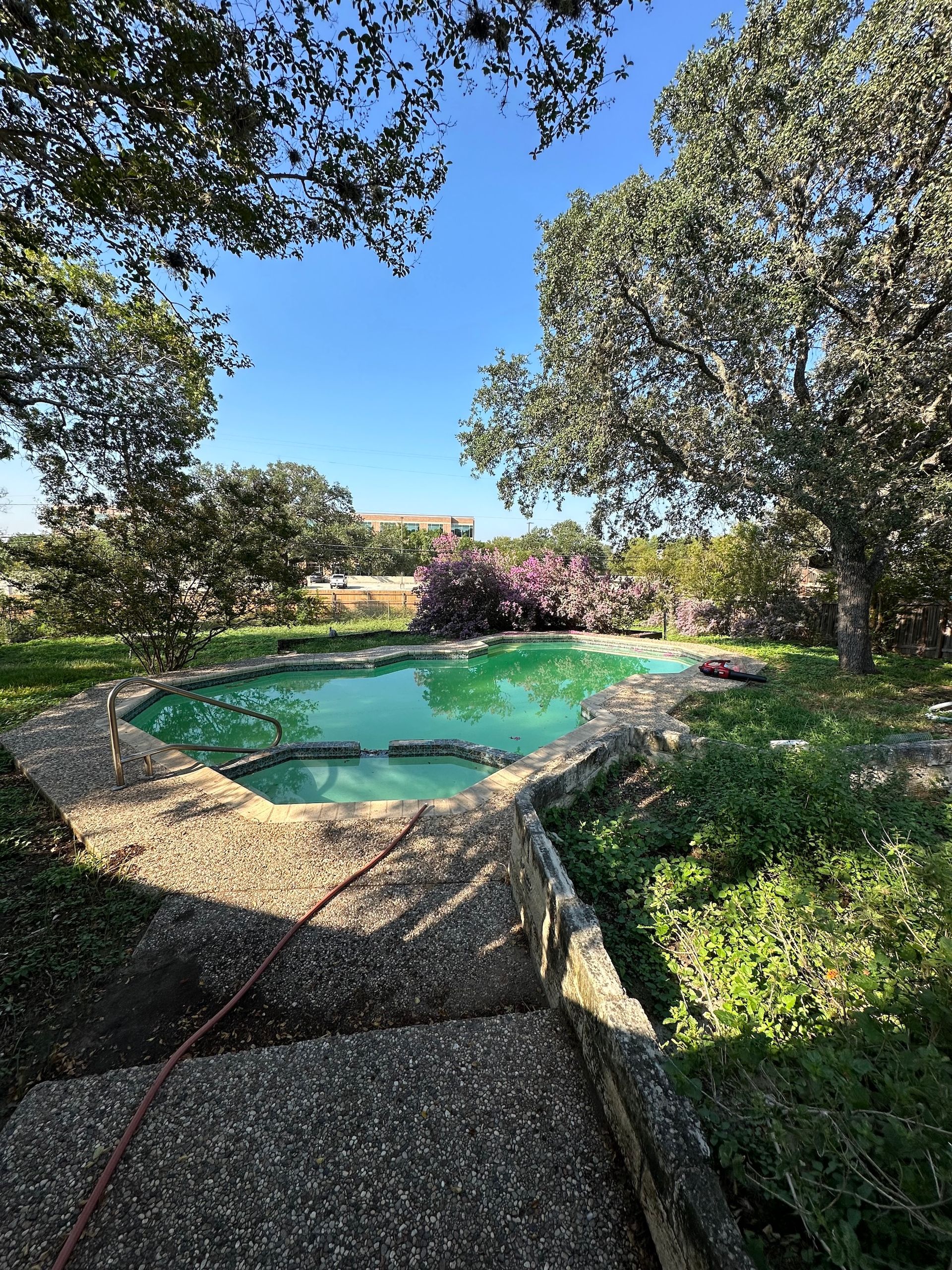 Stone-edged turquoise pool surrounded by trees and greenery under a clear blue sky