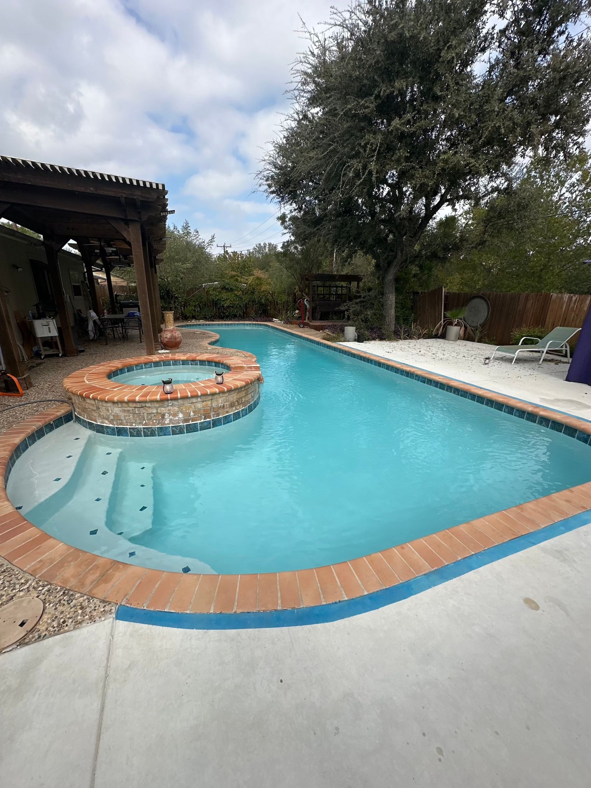 Backyard pool with a circular spa, blue water, and surrounding patio under trees