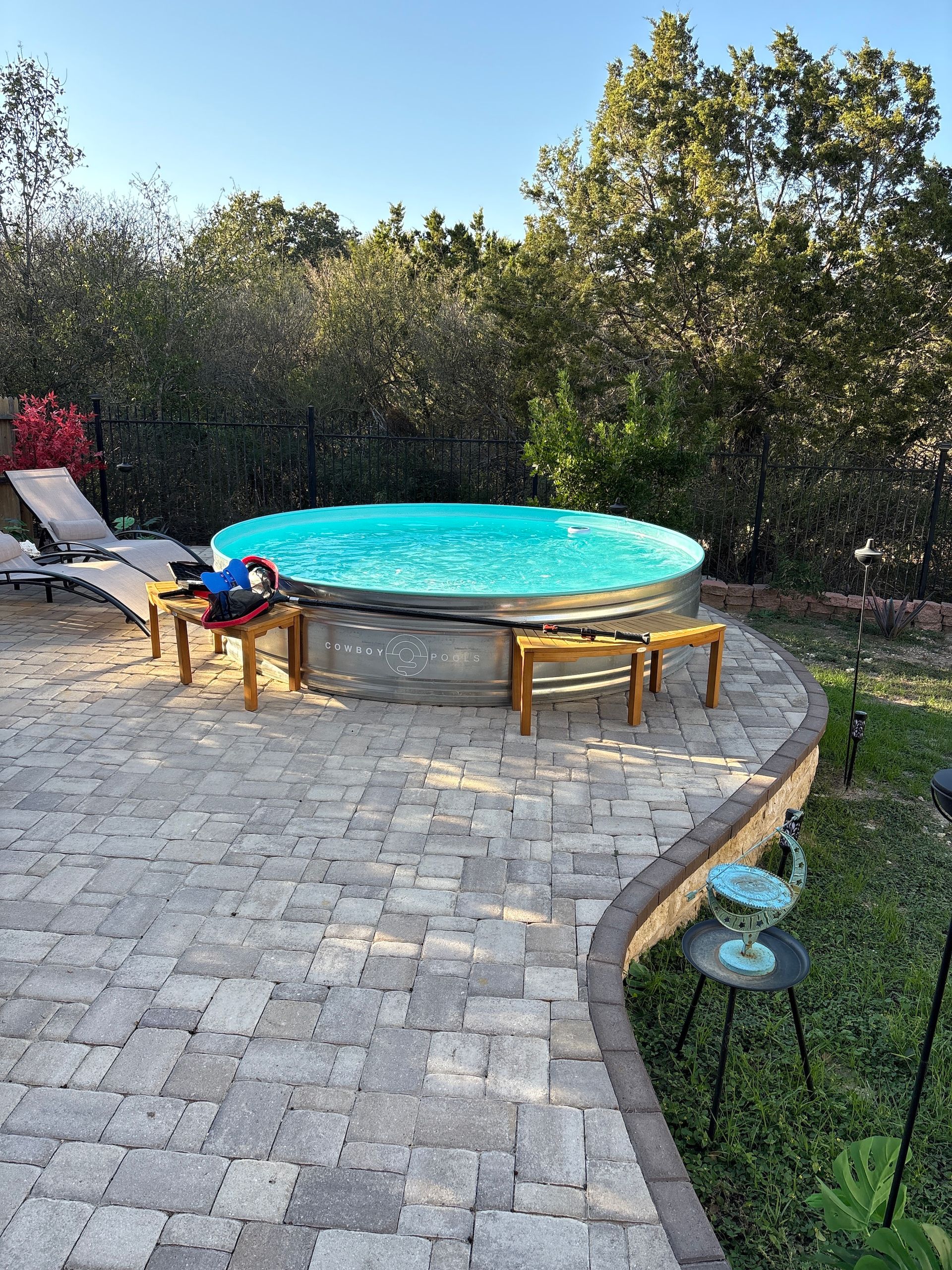 Backyard patio with a turquoise above-ground pool, lounge chairs, and potted plants