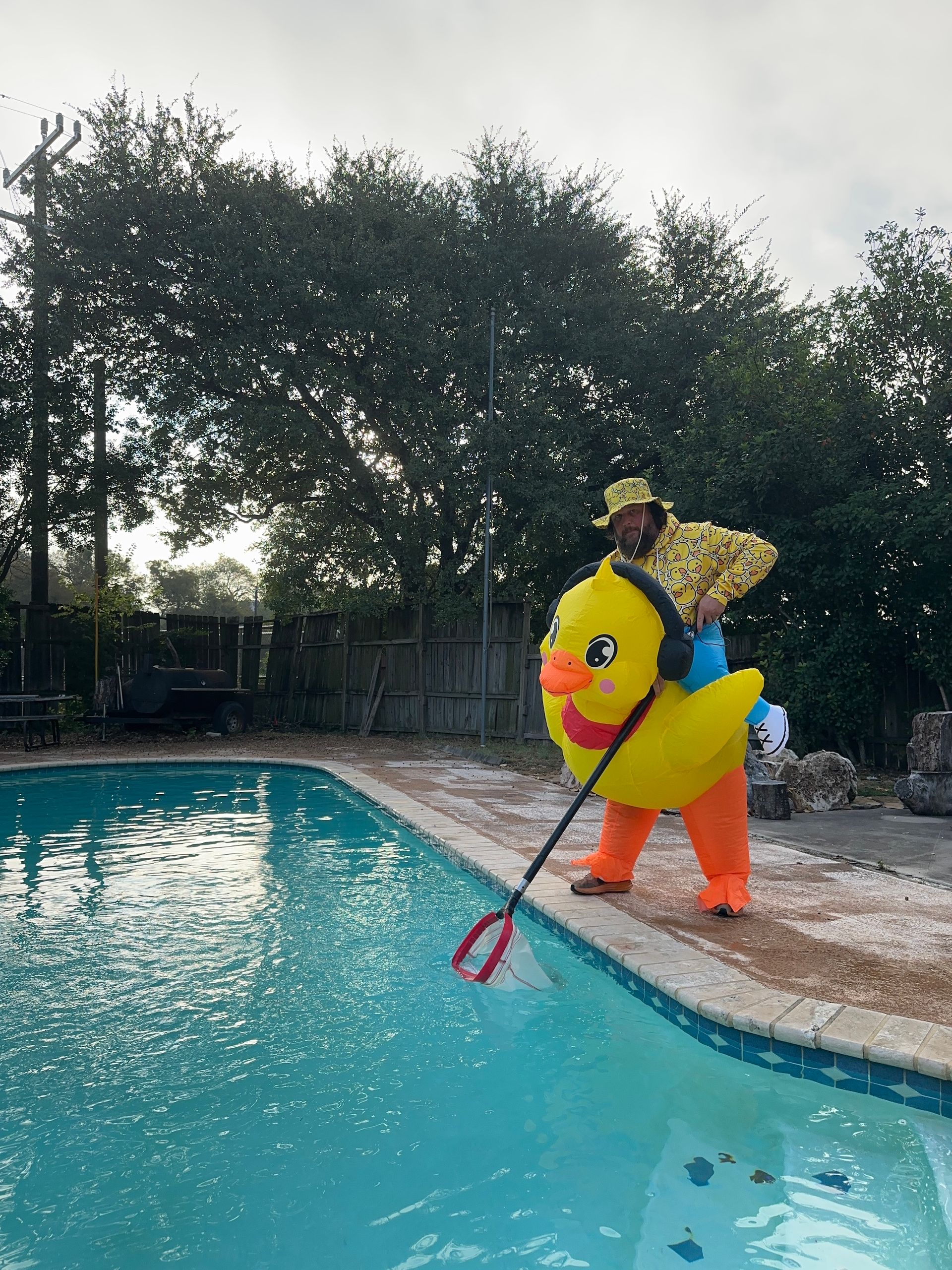 Person in a yellow duck float costume at a pool, holding a red net near the water.