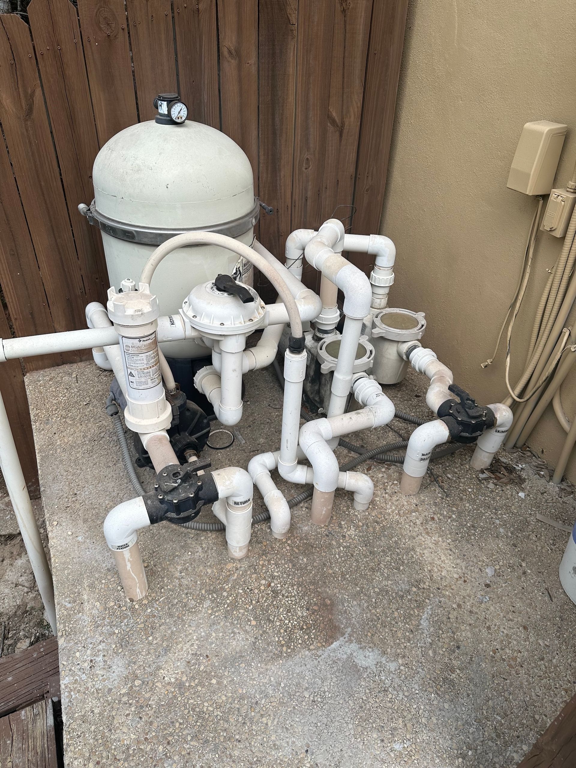 Pool filter and plumbing equipment beside a wooden fence outdoors