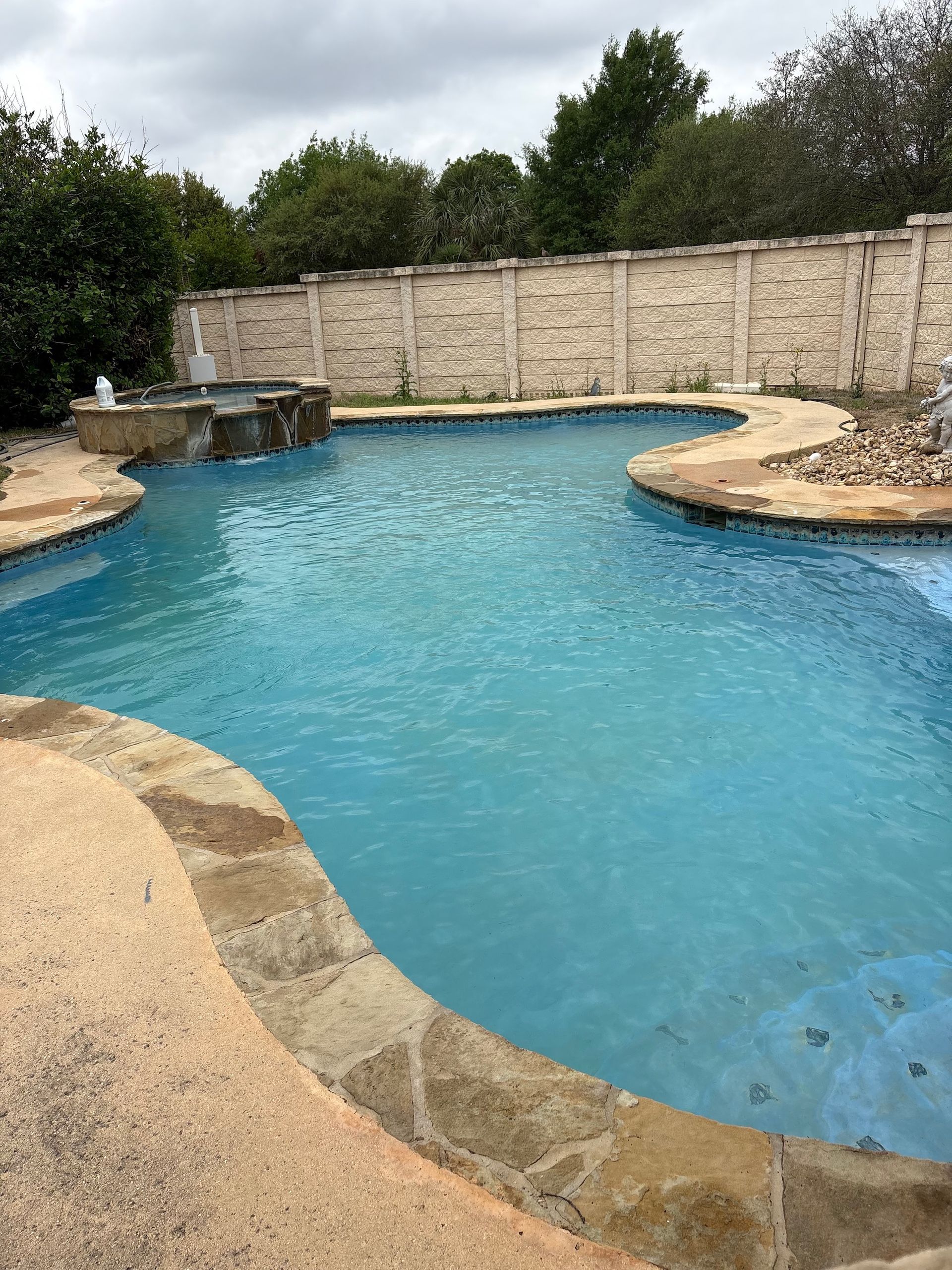 Backyard swimming pool with turquoise water, stone edging, and a beige privacy wall