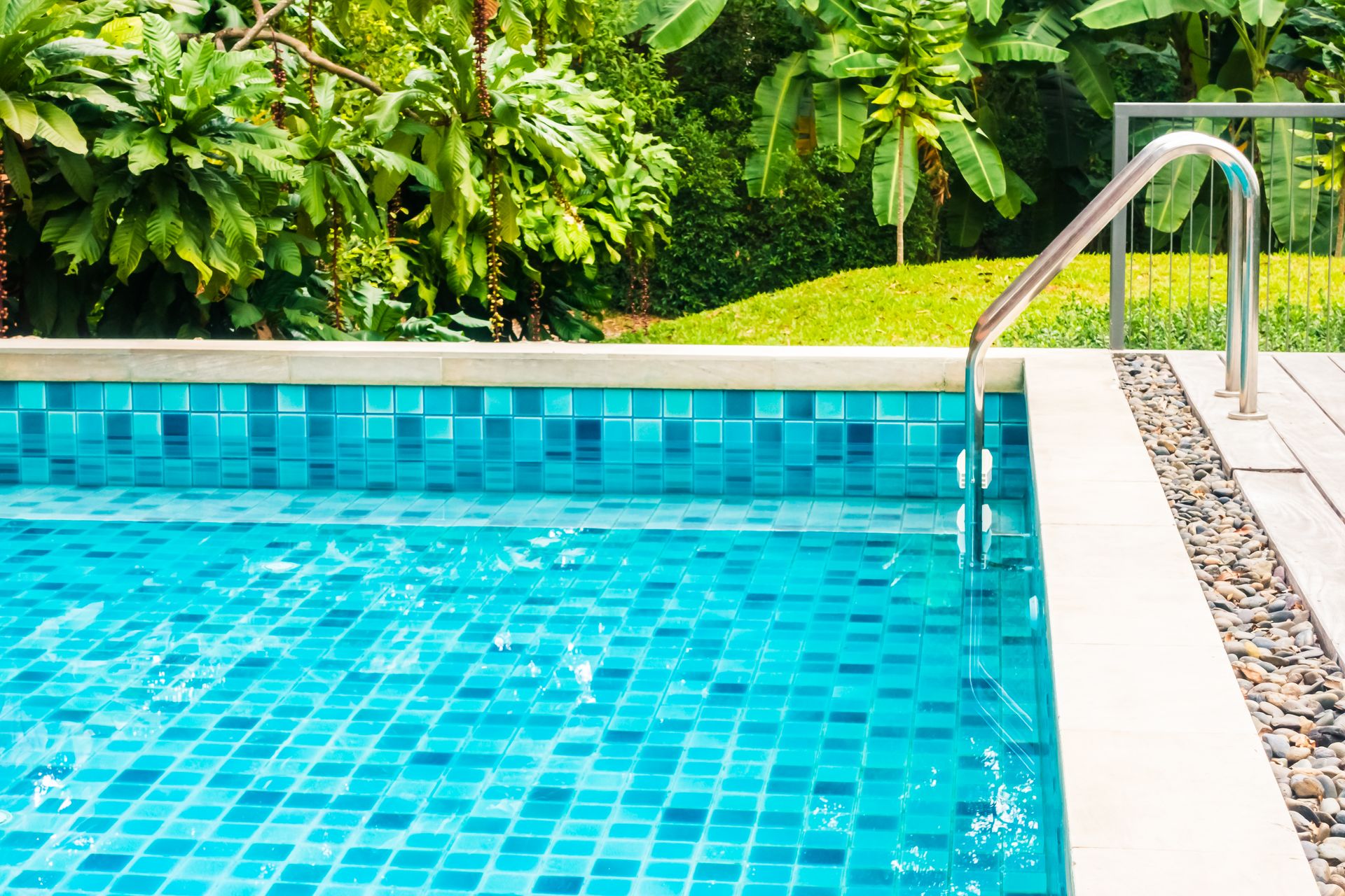 Outdoor swimming pool with turquoise water, white deck, and tropical plants along the edge