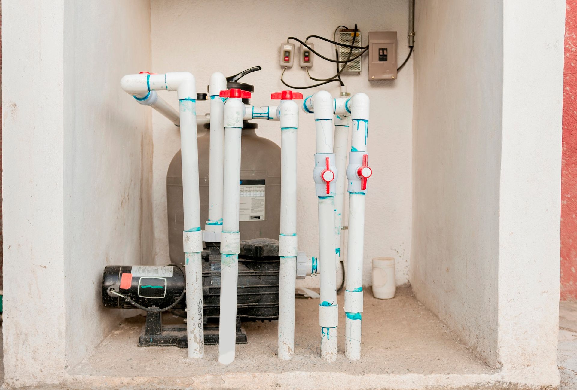 Pool equipment with pipes, valves, and filter tank beside a wooden fence.