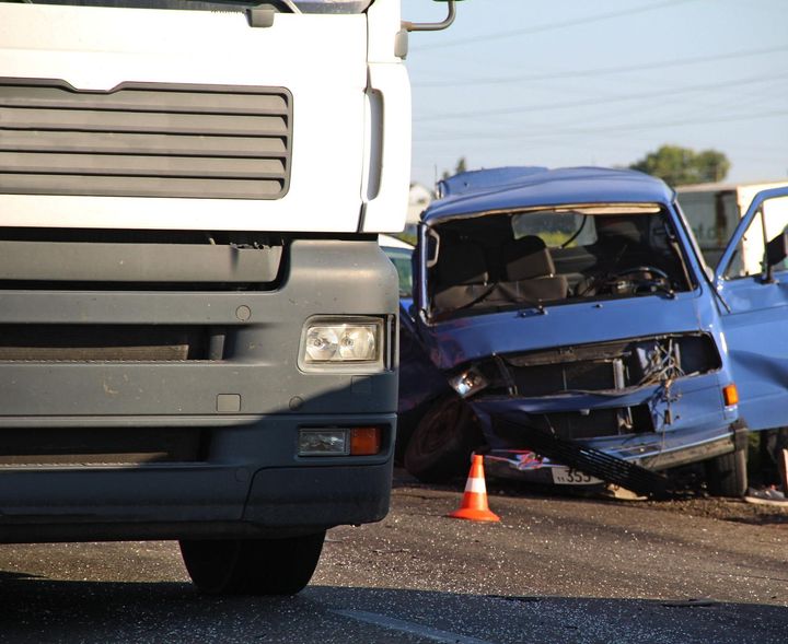 Blue car wrecked in crash with a white truck, debris and traffic cone on the road.