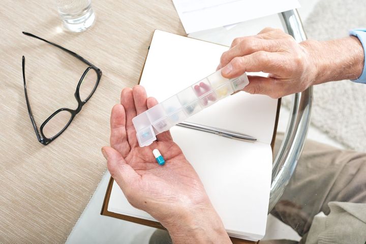 Hands holding a pill organizer over a table with eyeglasses and papers