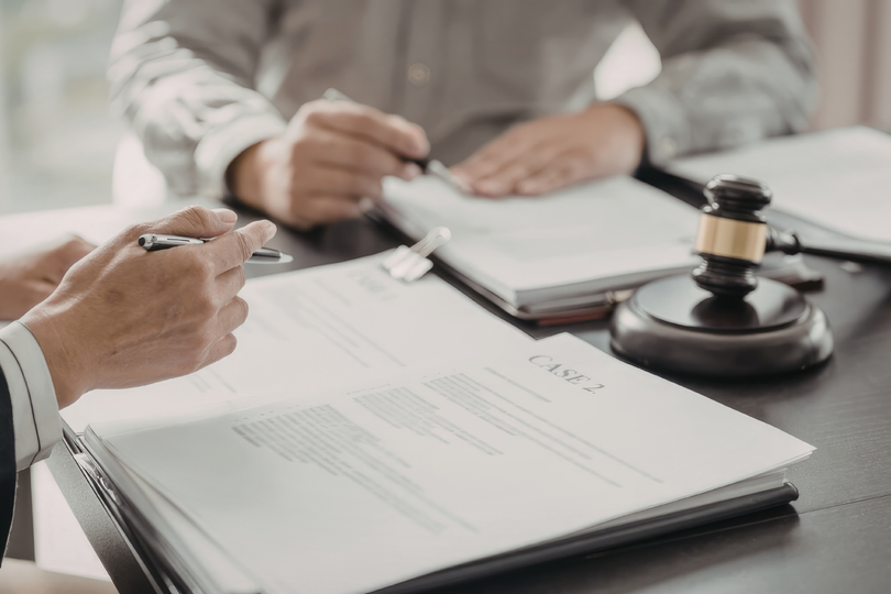 Hands signing legal documents at a desk with a judge’s gavel and notebook nearby