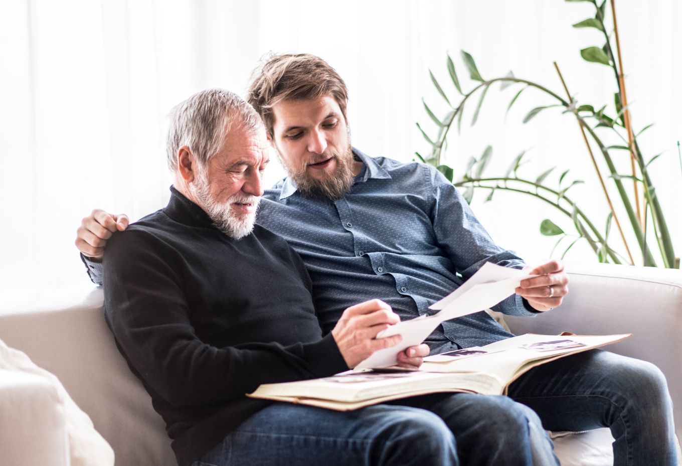 Two people sit on a couch reviewing papers together in a bright living room.