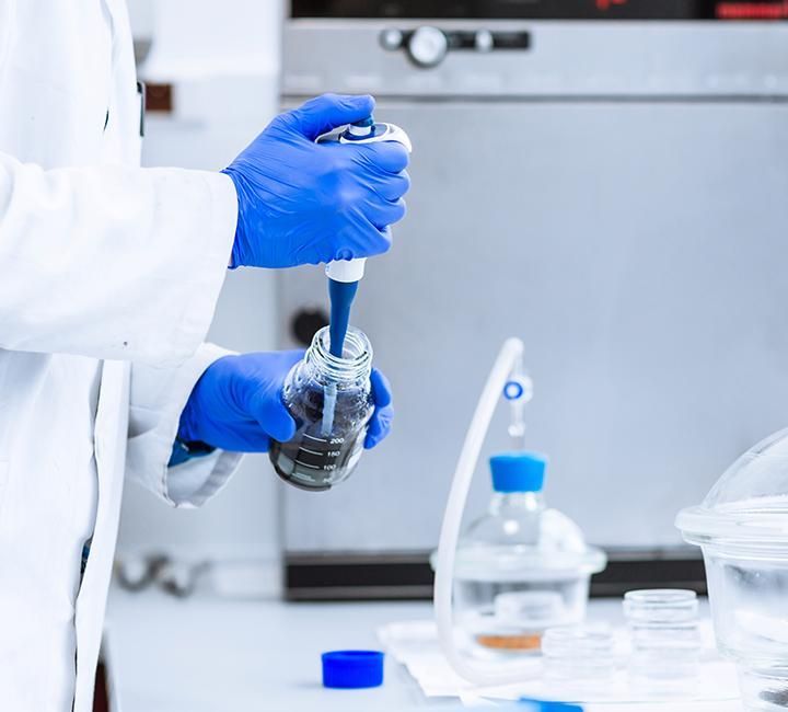 A person wearing blue gloves is holding a pipette and a bottle
