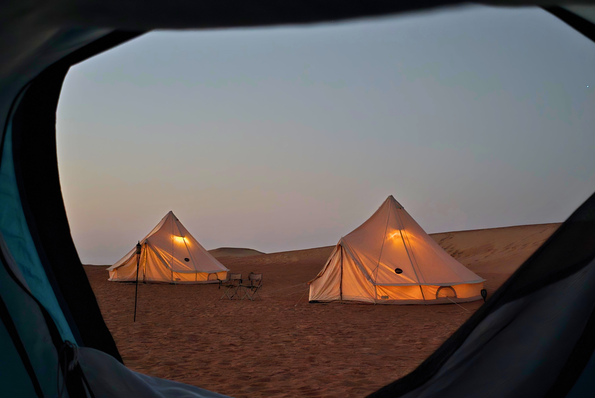 Two lit desert glamping tents at dusk, viewed through a tent in Abu Dhabi.