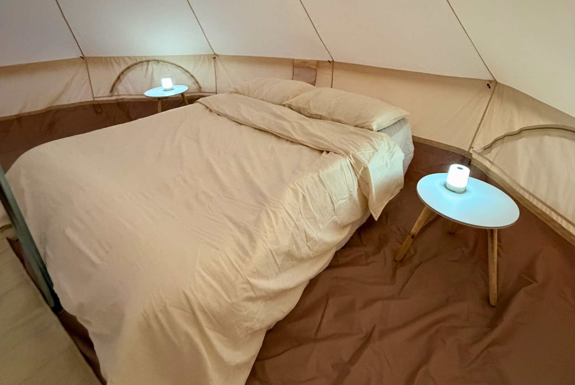 Cozy glamping tent bedroom with a bed, two small tables, and soft warm lighting in Al Quaa.