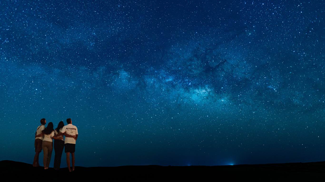 Three people standing on a dark horizon under a vivid starry blue night sky in Al Quaa.
