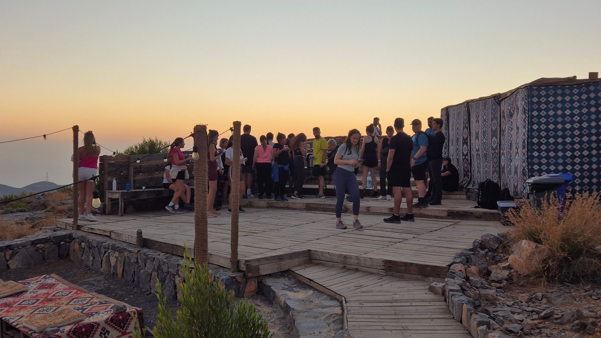 People standing on a rooftop terrace at sunset overlooking the sea in Jebel Jais' highest camp.