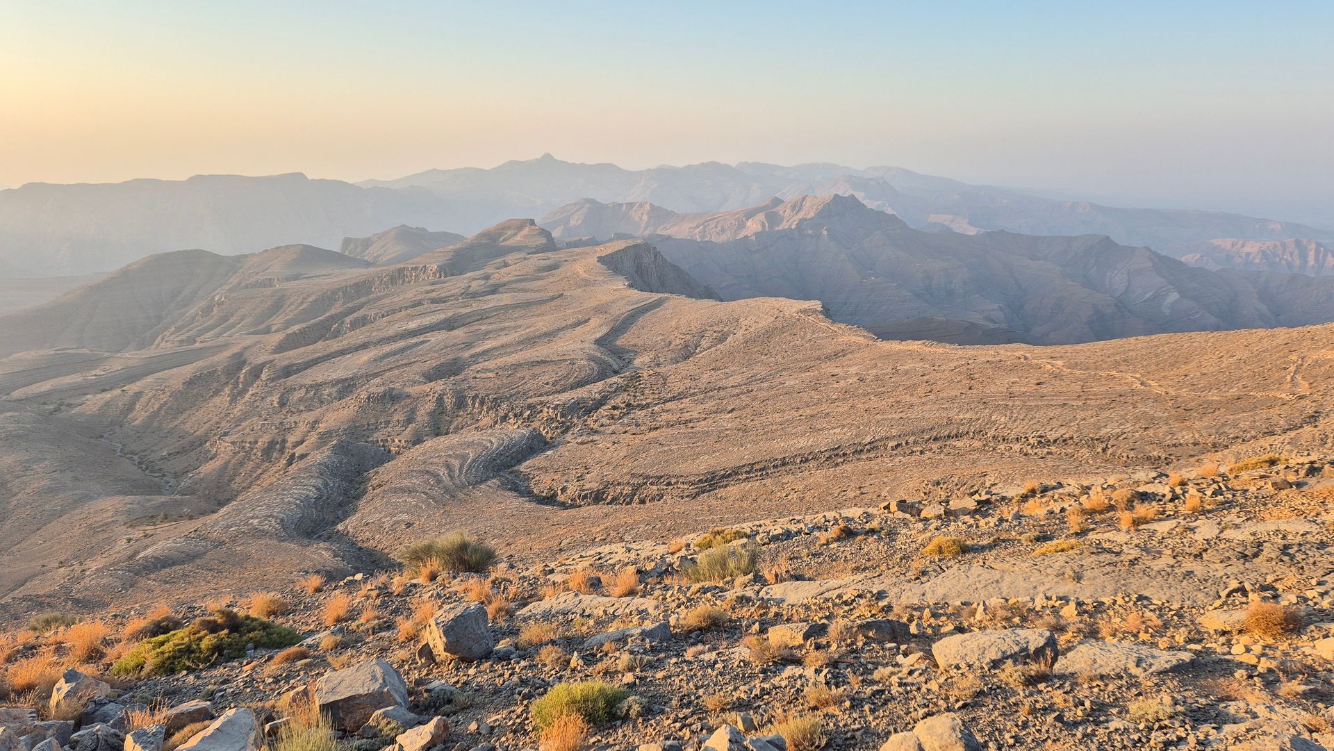 Rocky mountain ridge at sunrise with hazy distant peaks and warm golden light in Jebel Jais.