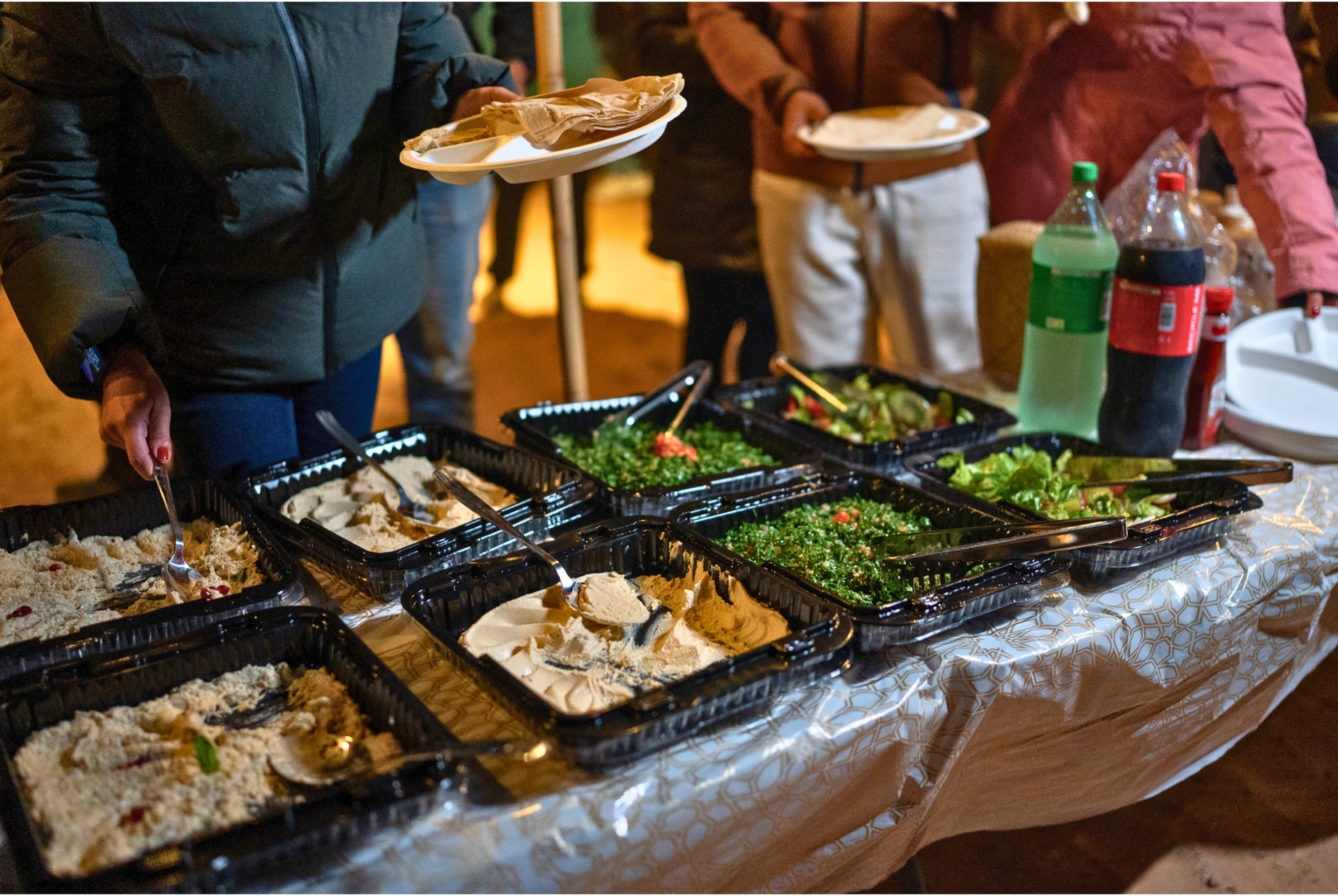 Outdoor buffet table with trays of food and drinks, with people serving themselves at a gathering