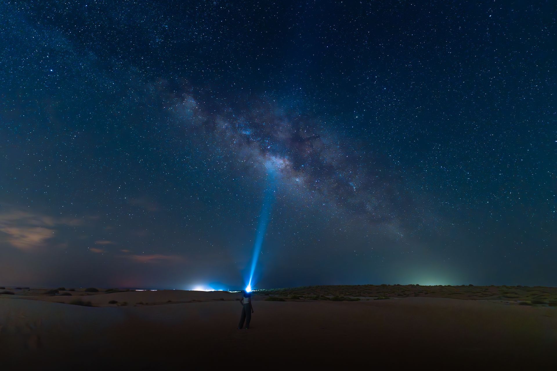 Person shining a blue light beam into a starry night sky in Al Quaa.