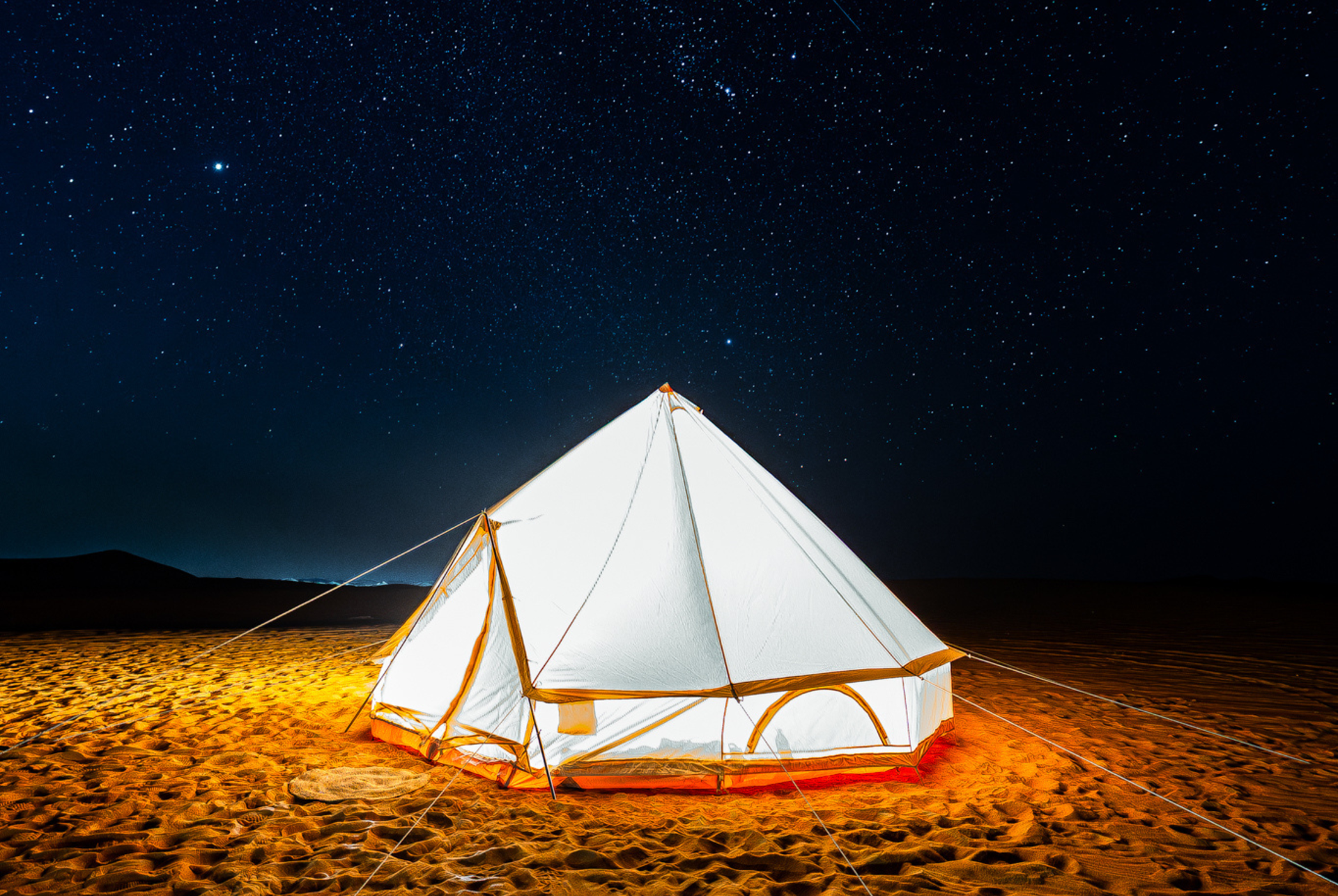 White glamping tent glowing on a sandy desert under a starry night sky in Al Quaa.