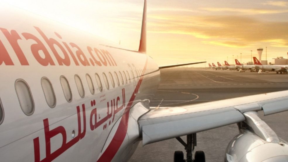 Air Arabia plane on airport tarmac at sunset, wing and logo visible