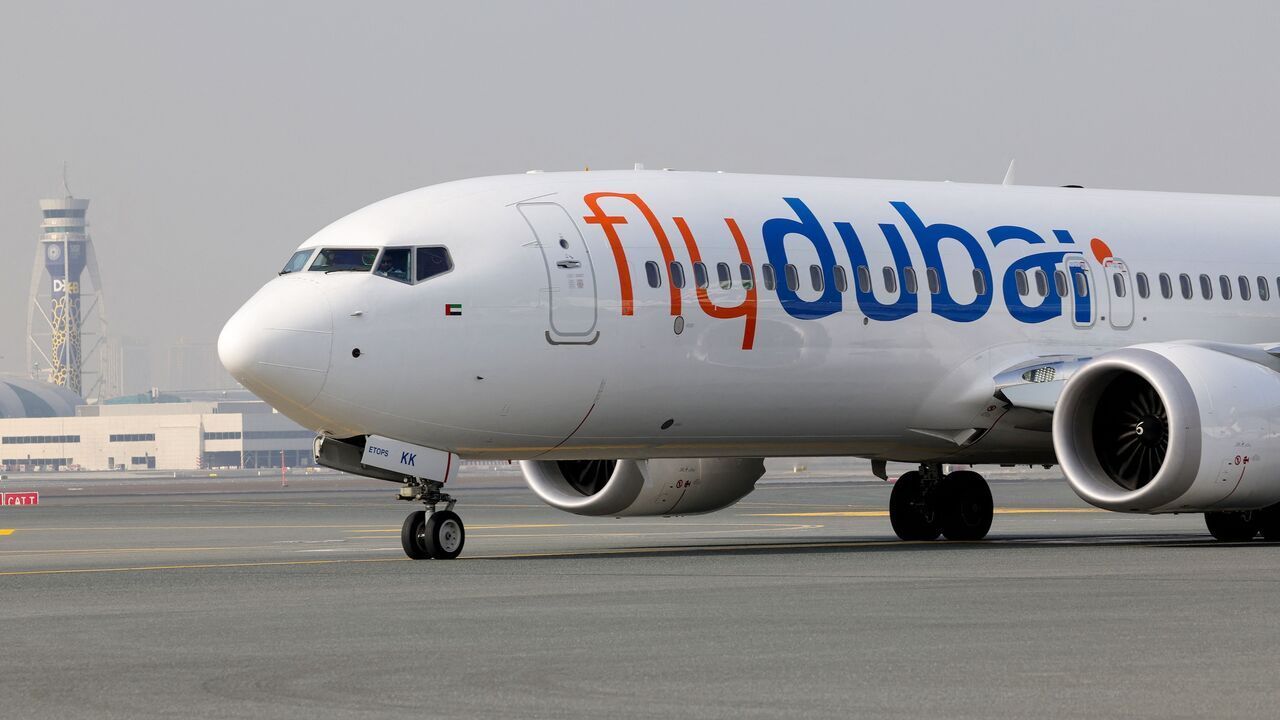 Flydubai airplane taxiing on a runway, white fuselage with orange and blue logo