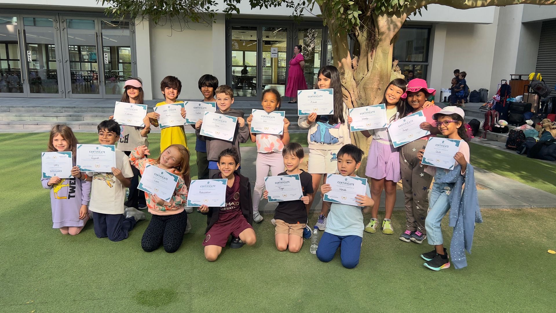 Hartland students holding certificates on a grassy lawn in front of the school's building.