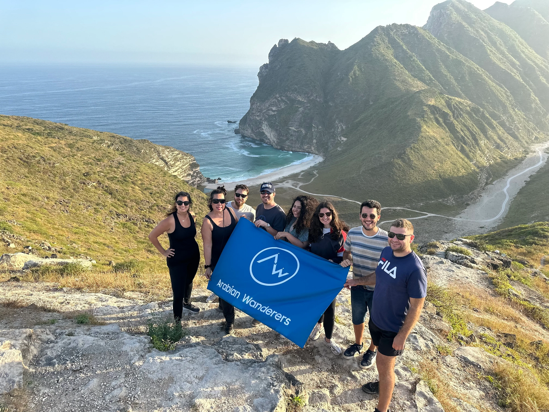 Group holding Arabian Wanderers' flag in front of the Hidden Beach Viewpoint in Dhofar.