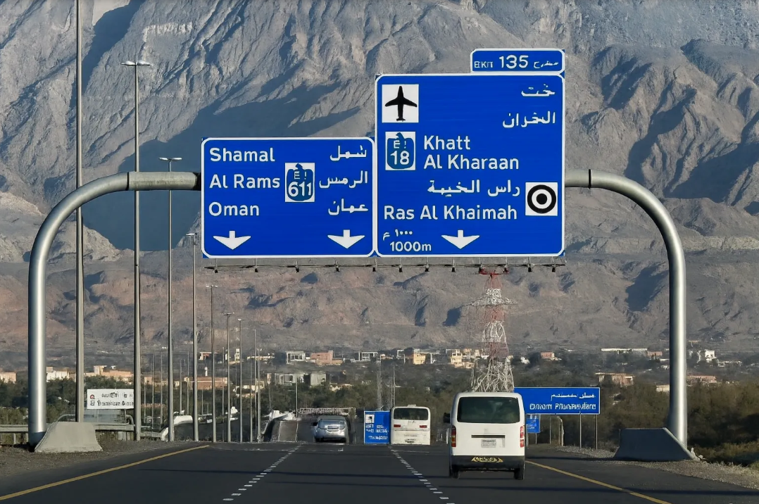 Highway road signs in Arabic and English against mountains, with a van on the road ahead.on the way to Jebel Jais