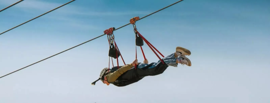 Person hanging upside down from a zipline against a clear blue sky in Jebel Jais.