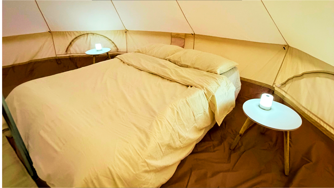 Inside an arabian wanderers glamping tent there is a double bed, cream bedding and two bedside lanterns