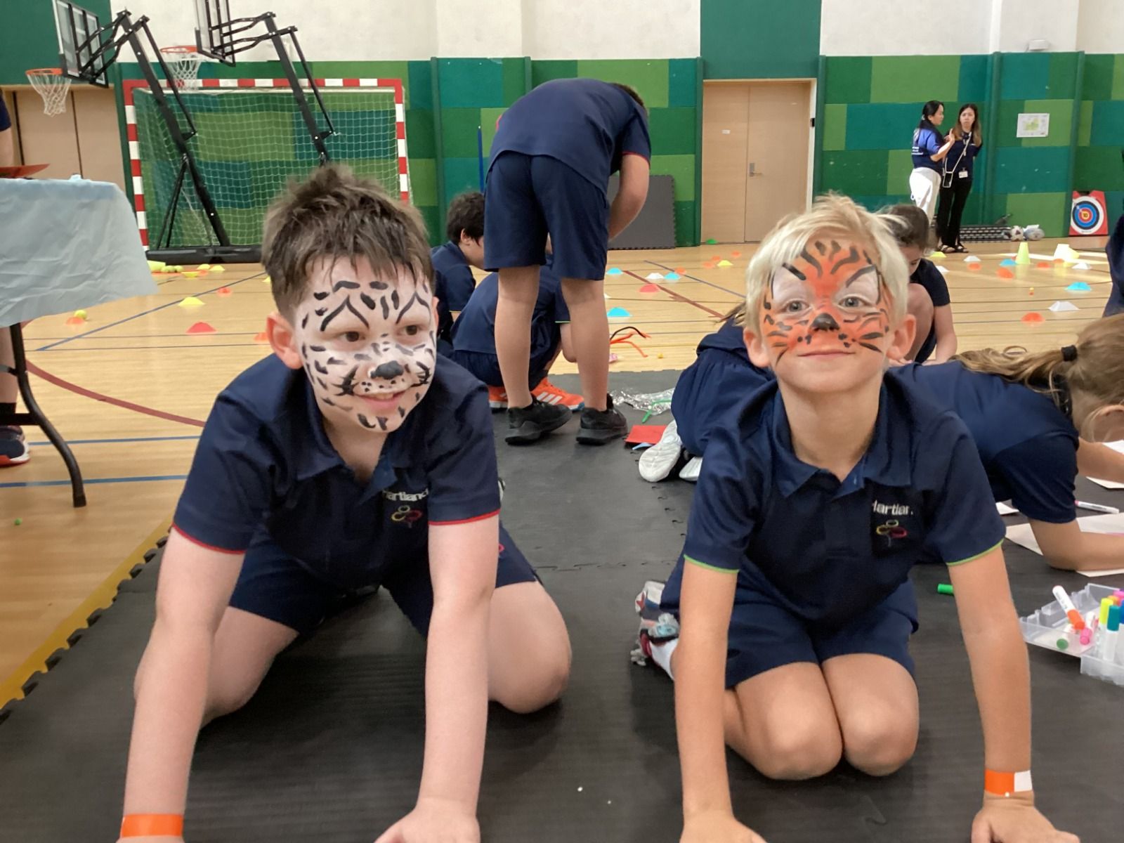 Two children with face paint kneel on a gym floor, with another child and play materials in the background in Hartland.