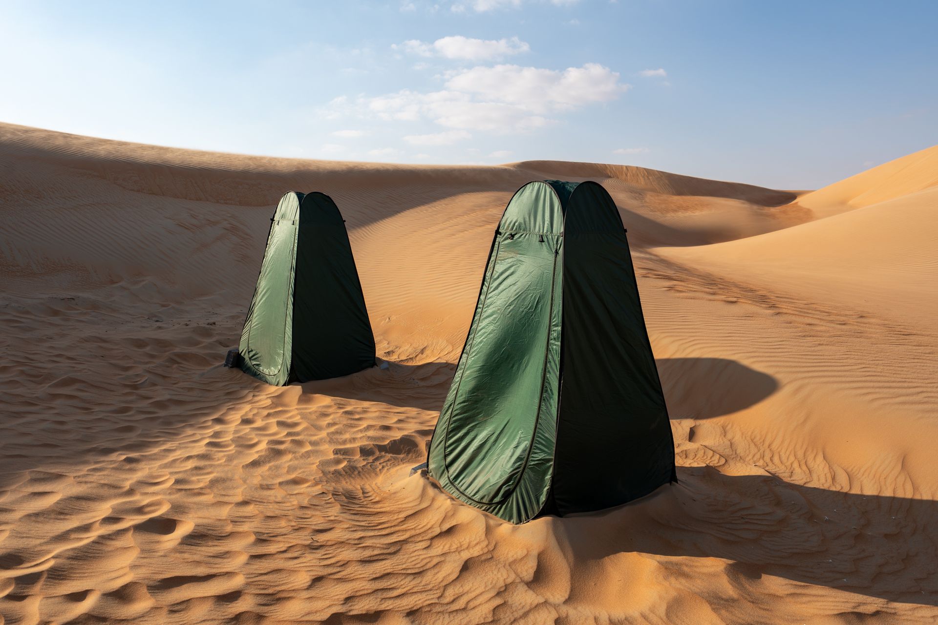 Two green toilet tents setup on sand dunes under a clear sky in Al Quaa.