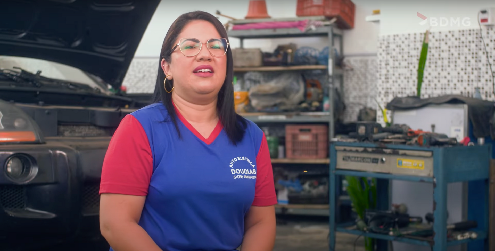 Uma mulher está parada na frente de um carro com o capô aberto em uma garagem.