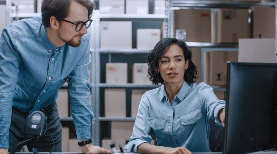 Um homem e uma mulher estão olhando para a tela de um computador em um armazém.
