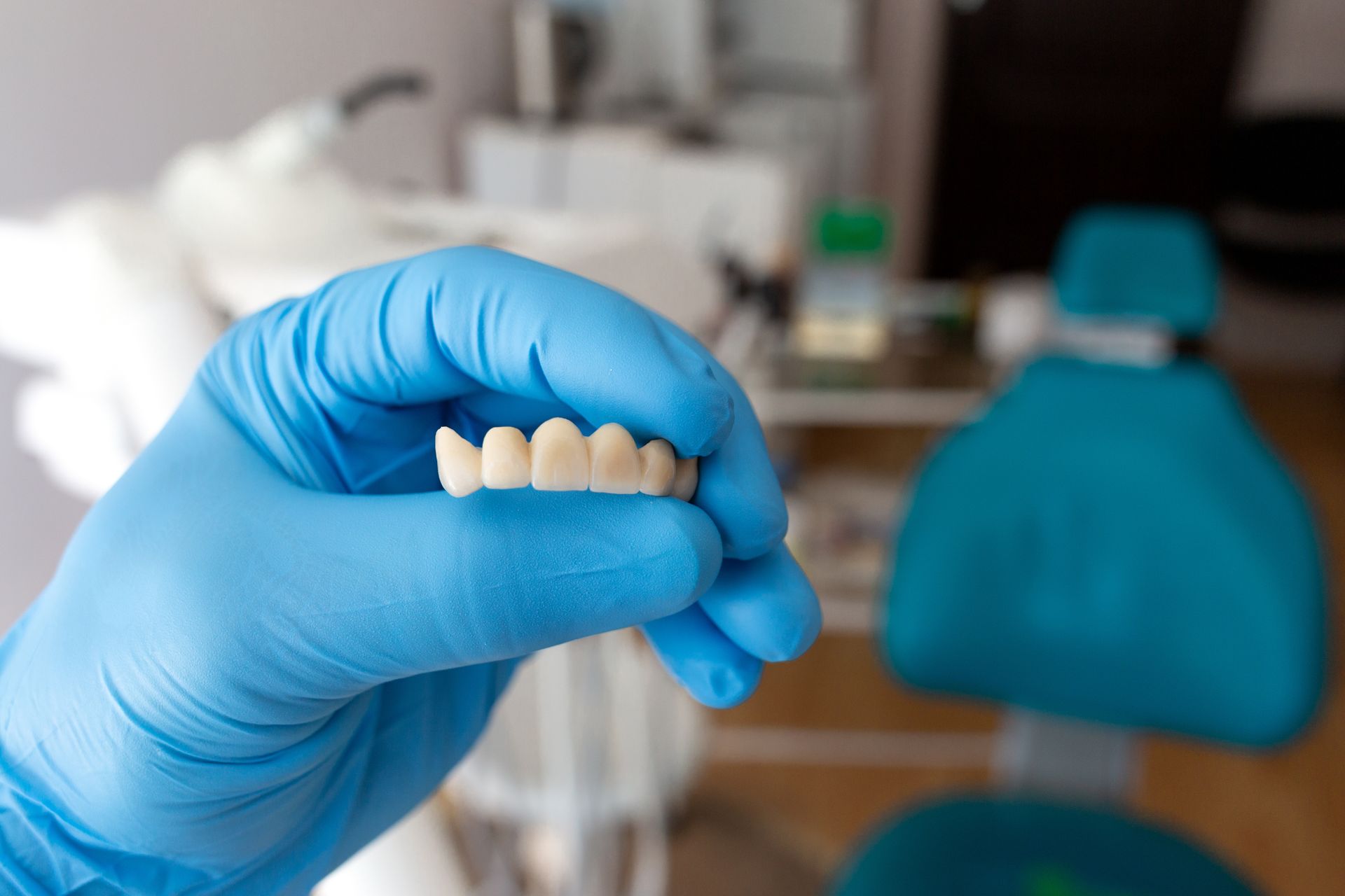 A person wearing blue gloves is holding a denture in their hand.