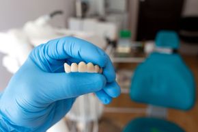A person wearing blue gloves is holding a denture in their hand.